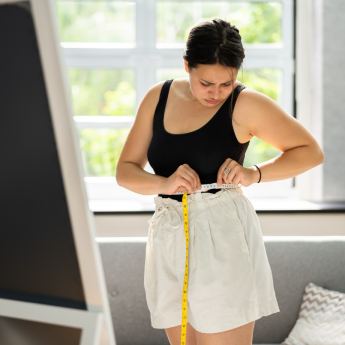 Women with tape measure around waist looking in mirror