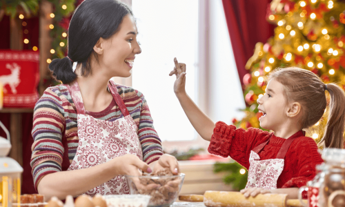 mom and daughter at table baking with christmas tree and lights in background