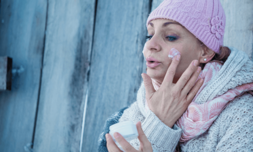 Women outside with winter clothes on putting lotion on face to prevent dry winter skin